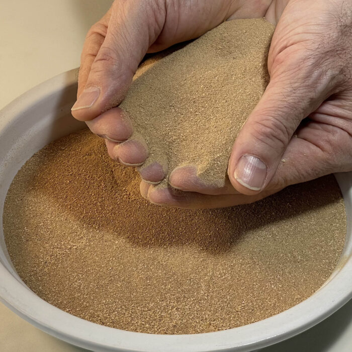 Two hands holding mealworm frass over a bowl filled with mealworm frass